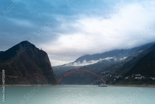 The red Wushan Yangtze River Bridge is breathtakingly beautiful, gracefully spanning the river against a backdrop of cloud-covered mountains. photo