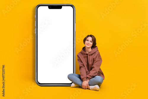 Full size cadre of young promoter woman sit near smartphone interface screen instruction download app isolated on yellow color background