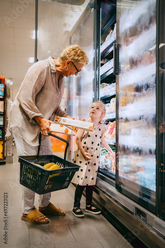 Senior woman holding basket while buying groceries with granddaughter at store photo