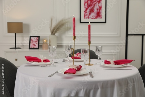 Color accent table setting. Glasses, plates, burning candles and pink napkins on table in dining room photo
