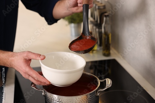 Man pouring delicious tomato soup into bowl in kitchen, closeup