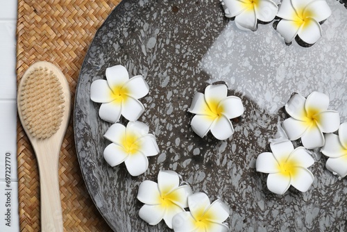 Bowl of water with plumeria flowers and brush on table, top view. Spa treatment