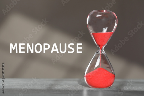 Menopause word and hourglass on table against grey background