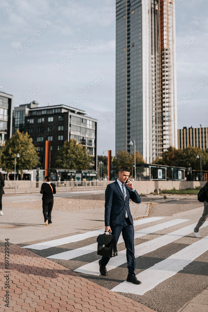 Businessman talking through smart phone while walking on zebra crossing at street in city Businessman talking through smart phone while walking on zebra crossing at street in city