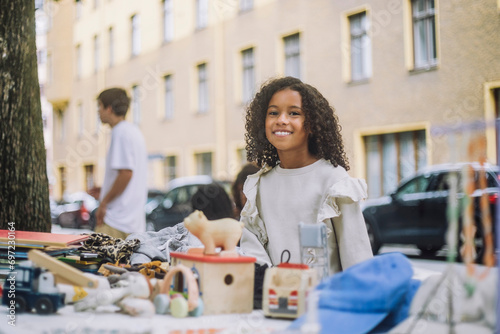 Portrait of smiling elementary girl standing near stall at flea market photo