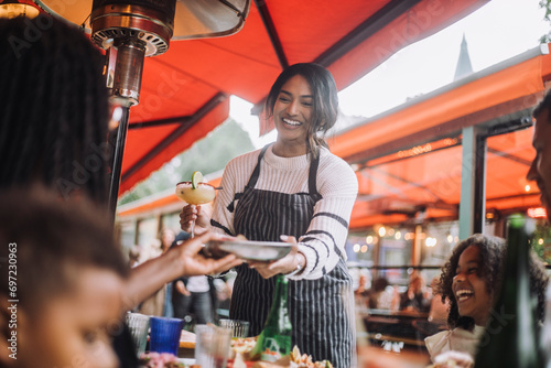 Smiling waitress serving food and drinks to customers having fun at restaurant