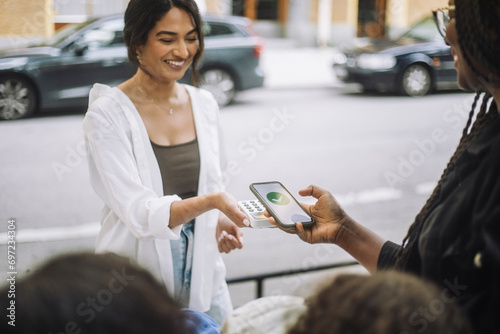 Smiling female vendor taking online payment from customer while selling at market photo