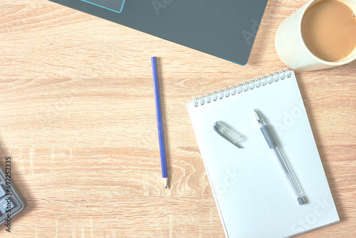 an open notepad for notes, a fountain pen, a pencil calculator, a cup of coffee and a laptop on a wooden table with a copy space, top view