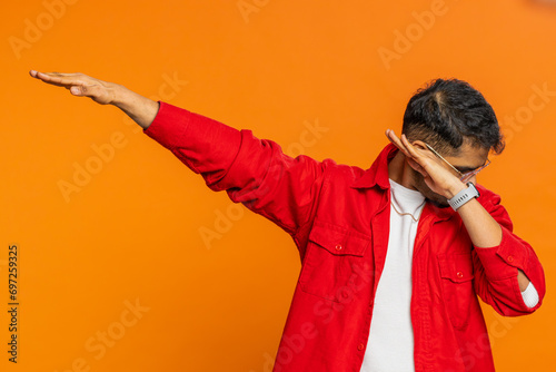 Trendy cheerful positive Indian man having fun dancing and moving to rhythm, dabbing raising hands, making dub dance winner celebrating victory gesture. Happy Arabian guy isolated on orange background photo