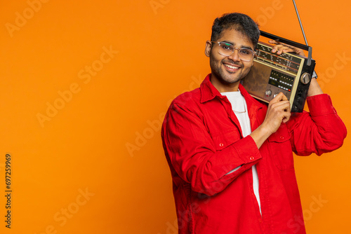 Happy young Indian man using retro tape record player to listen music, disco dancing favorite track, having fun entertaining, fan of vintage technologies. Arabian guy on orange background. Copy-space