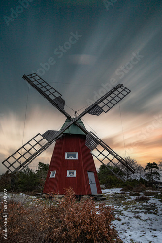 Typical historical red wooden windmill in a winter landscape. Sunset on the coast on a rock. Stenungsund in Sweden photo