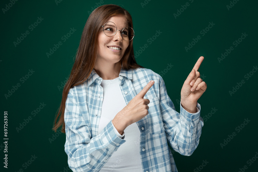 Young pretty woman with brown hair points her finger to the side on a dark green background Young pretty woman with brown hair points her finger to the side on a dark green background