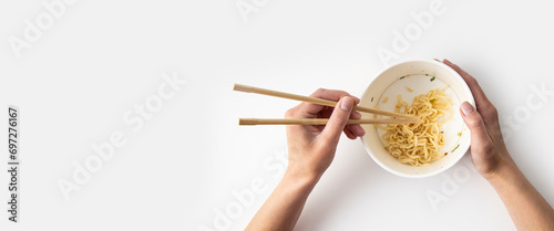 Female hand takes Chinese noodles with Chinese chopsticks from a paper bowl on a white background. Top view, fly lay. Banner photo