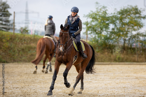 Horse during training with rider on the riding arena, galloping in a turn, photographed from the front in the background by another rider.