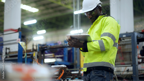 A black African engineer holding a digital tablet is inspecting the operation of a machine at Plastic factory.