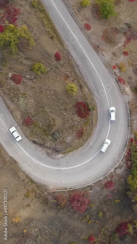 Cars go on turn of serpentine mountain road. Aerial vertical top view. Vertical Video