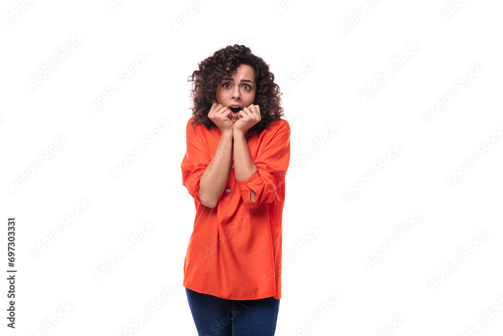 young caucasian brunette woman with curly hair dressed in an orange blouse feels surprised