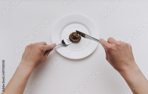 Two female hands hold a stainless steel knife and fork near the plate and cut artificial feces. Fake news, jokes. Concept of inept chef, lousy restaurant, bad food, crappy taste. photo