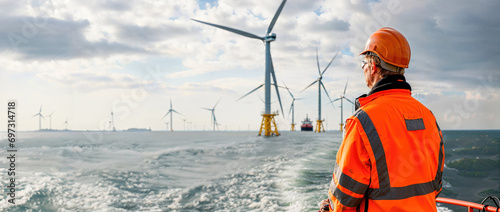 A worker in reflective gear looks at wind turbines at sea, symbolizing the use of renewable energy and sustainable practices.