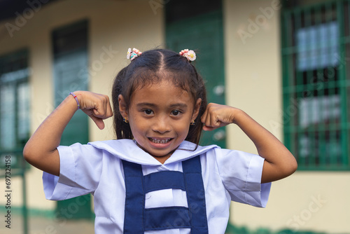 A confident preschooler asian lady flexes her arms. A little girl at a provincial primary school in Bohol.