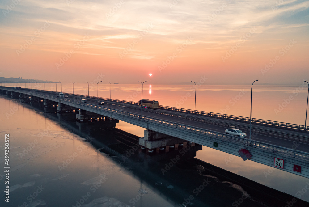 Aerial drone view of low-water bridge across the bay with moving car during the sunset. Active movement of transport cars vehicles in different directions.