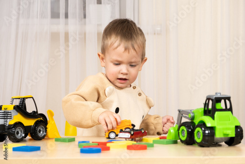 Little cute boy playing with toys while sitting at table