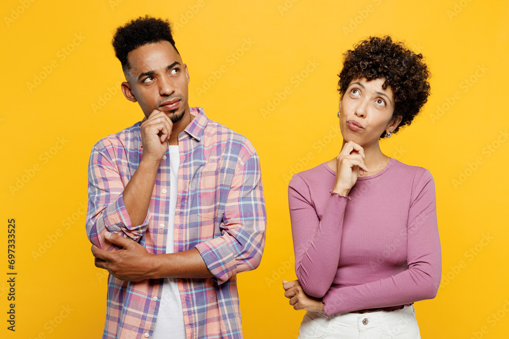 Young couple two friend family man woman of African American ethnicity wear purple casual clothes together put hand prop up on chin lost in thought and conjectures isolated on plain yellow background Young couple two friend family man woman of African American ethnicity wear purple casual clothes together put hand prop up on chin lost in thought and conjectures isolated on plain yellow background