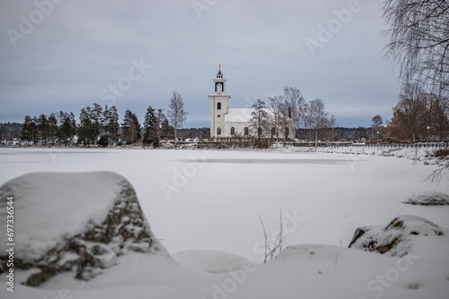 Swedish houses, small white church by a lake in a cold winter landscape with snow and ice. Vårviks kyrka in Sweden photo