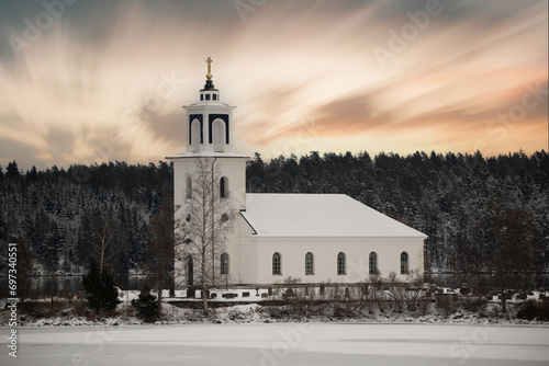 Swedish houses, small white church by a lake in a cold winter landscape with snow and ice. Vårviks kyrka in Sweden photo