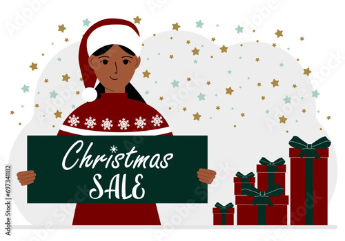 A woman in a sweater and a red Santa hat holds a poster with the text about Christmas sale in his hand.