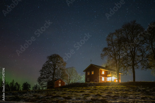 Winter landscape with wooden house under a beautiful starry sky and Northern Lights © Jan