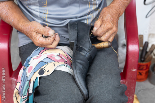 A shoe maker sewing a black leather shoe with weathered hands.  photo