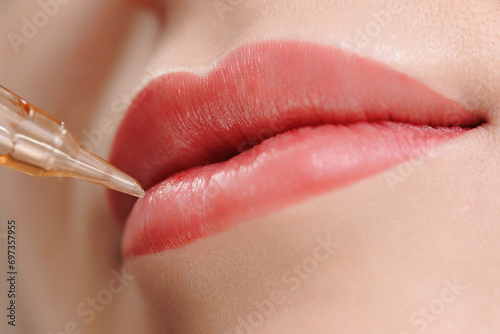 Procedure permanent makeup in beauty salon, tattoo machine with red pigment on woman lips photo