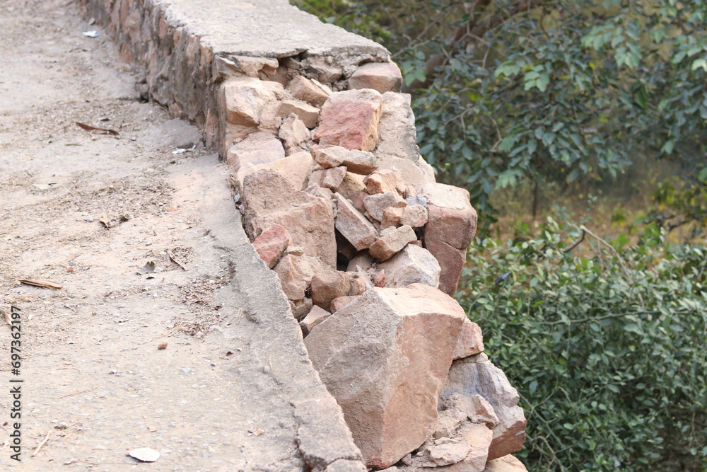 Closeup of a Broken and damaged stone wall and stone pillar in selective focus in Trees bokeh Bhondsi, Pandala with green vegetation in background Closeup of a Broken and damaged stone wall and stone pillar in selective focus in Trees bokeh Bhondsi, Pandala with green vegetation in background