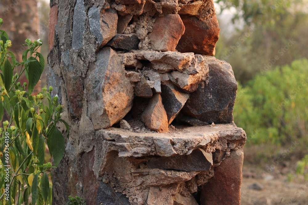 Fototapeta premium Closeup of a Broken and damaged stone wall and stone pillar in selective focus in Trees bokeh blur