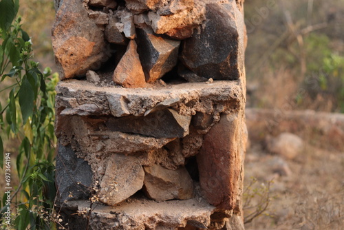 Closeup of a Broken and damaged stone wall and stone pillar in selective focus in Trees bokeh, thick wall photo