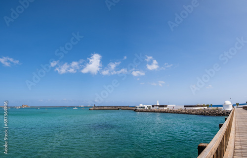 View of the Fermina islet and wooden access bridge. Turquoise blue water. Sky with big white clouds. Seascape. Lanzarote, Canary Islands, Spain. © Jess