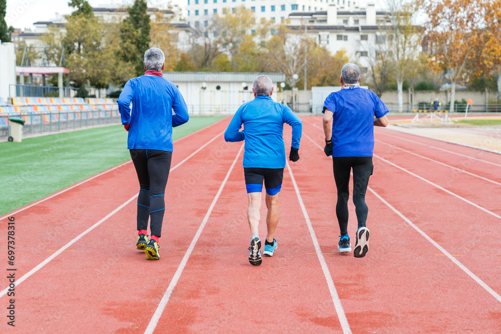 Three senior male runners in blue sportswear train on an athletic track, showcasing active lifestyle and teamwork in sports.