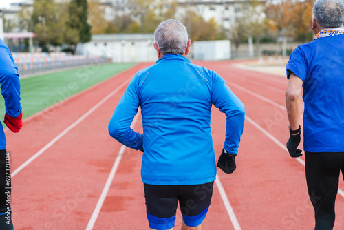 Three senior male athletes in blue stand poised on a running track, showcasing active lifestyle and fitness in old age.