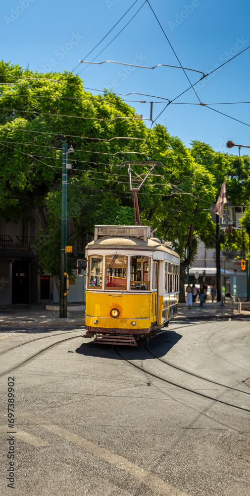 Fototapeta premium Famous and typical old yellow tram, beautifully decorated and preserving the original designs traveling uphill on the tracks of a typical Lisbon street in Portugal.