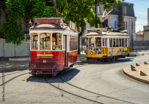 Famous and typical vintage old red tram, beautifully decorated and retaining the original designs running on the tracks in a typical Lisbon street in Portugal. Behind him is another yellow tram.