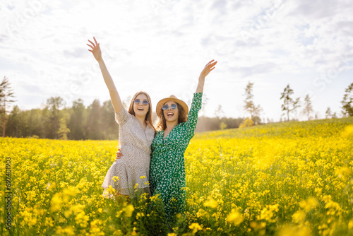 Two young happy women in the middle of a yellow rapeseed field. Girlfriends having fun outdoors on a sunny day. Concept of fun, relaxation. Lifestyle.