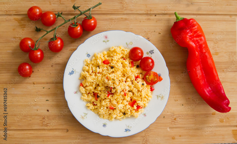 Leckeres Frühstück, Rührei mit Tomaten und Paprika auf einem weißen Blumenteller auf einem rustikalen Holztisch Leckeres Frühstück, Rührei mit Tomaten und Paprika auf einem weißen Blumenteller auf einem rustikalen Holztisch