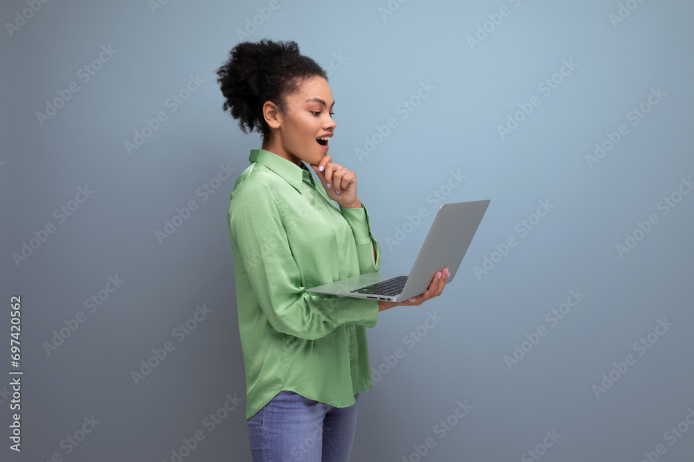 young brunette hispanic woman with curly hair in green rejoices holding a laptop in her hand against the background with copy space young brunette hispanic woman with curly hair in green rejoices holding a laptop in her hand against the background with copy space