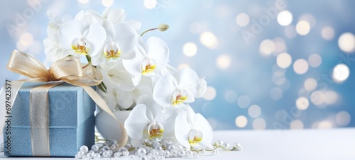 Beautifully wrapped gift box adorned with a golden ribbon bow, accompanied by white orchids. Banner with copy space. Ideal for greeting, postcard for Womens day, Valentines day or special occasions © Jafree