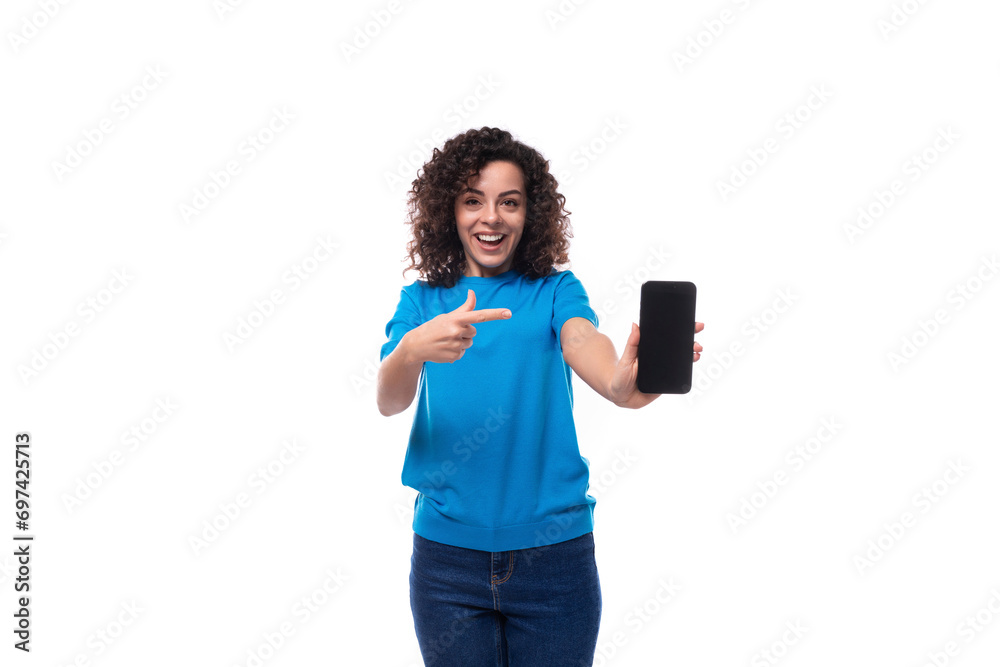 young woman with curls dressed in a blue t-shirt shows the screen of a mobile phone with a mockup young woman with curls dressed in a blue t-shirt shows the screen of a mobile phone with a mockup