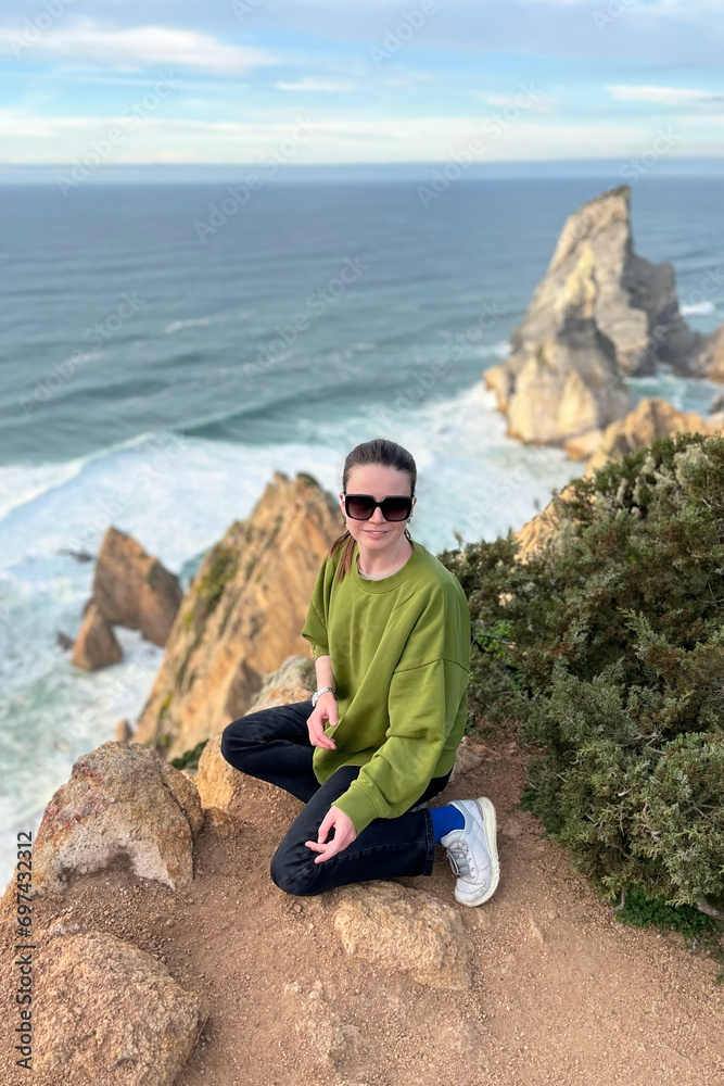 Young woman meditating in front of the cliffs on the Atlantic ocean in Portugal