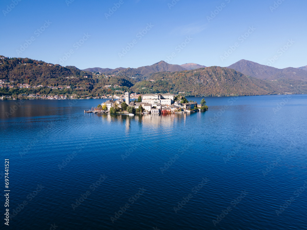 San Giulio Island within Lake Orta in Piedmont, Italy. aerial drone view in autumn. mountains, blue water and reflection