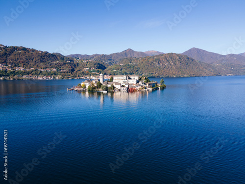 San Giulio Island within Lake Orta in Piedmont, Italy. aerial drone view in autumn. mountains, blue water and reflection © Andrea