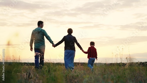 Family takes stroll along valley relishing landscape as sun set over horizon. Family walks on grassy valley. Family shares tranquil evening walking in verdant meadow immersed in beauty of surroundings